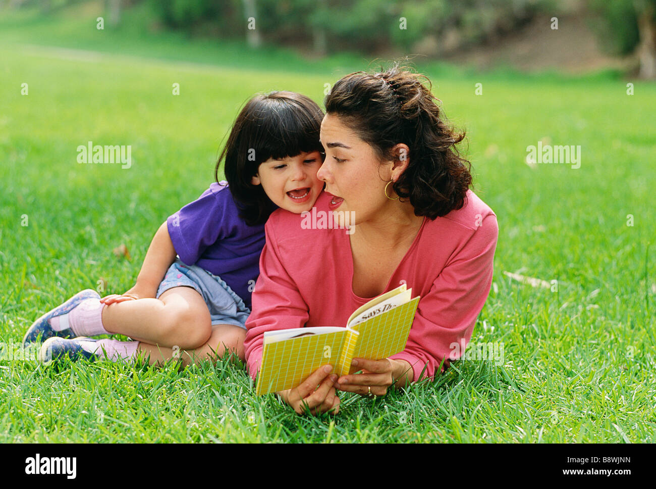 Latina-Mutter und Tochter ein Buch draußen auf dem Rasen. Stockfoto