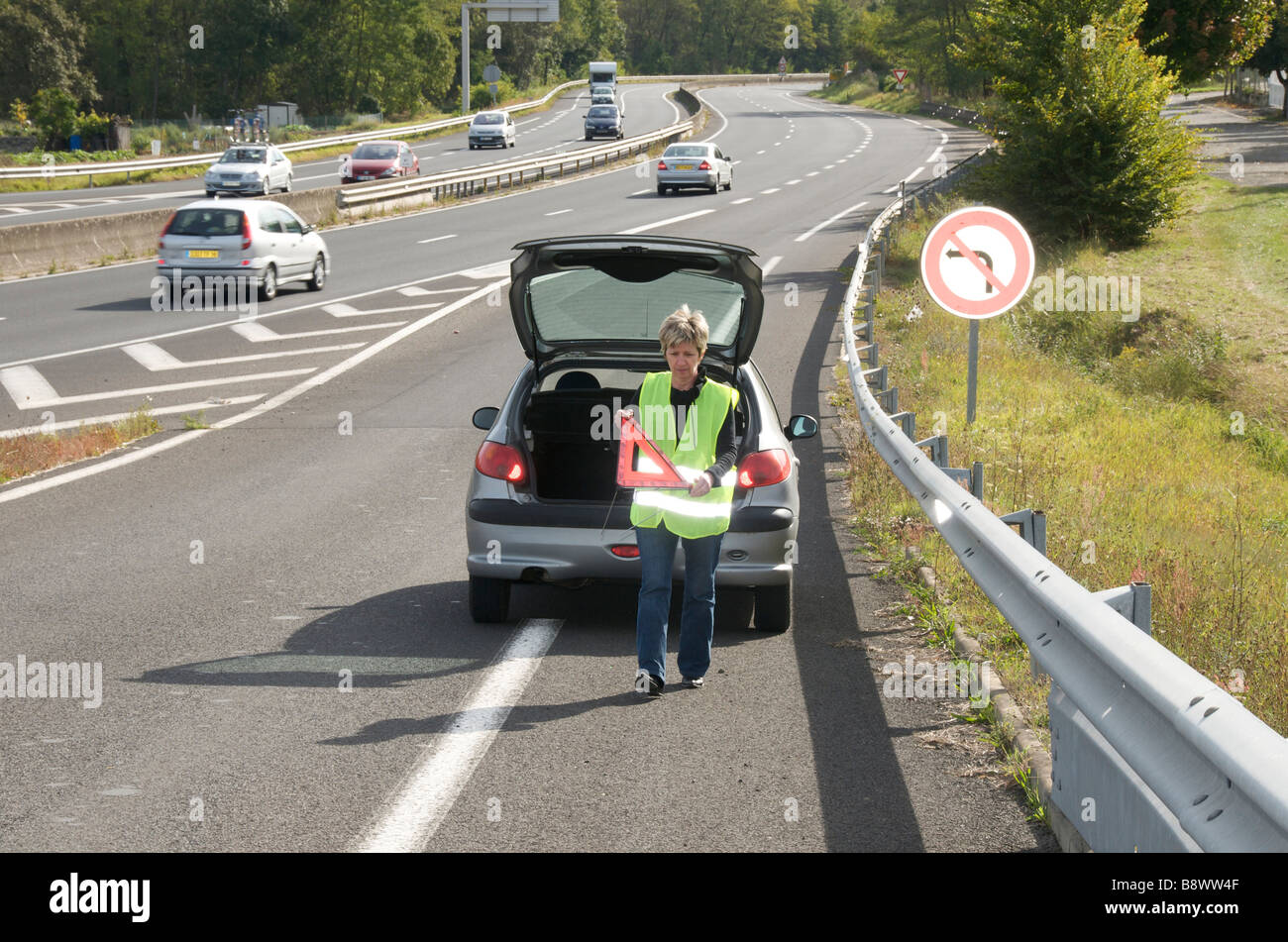 Frau ihr rotes Warndreieck platzieren melden Sie hinter ihrem aufgeschlüsselt Auto auf einer Ausfahrt auf einer französischen Autobahn Stockfoto
