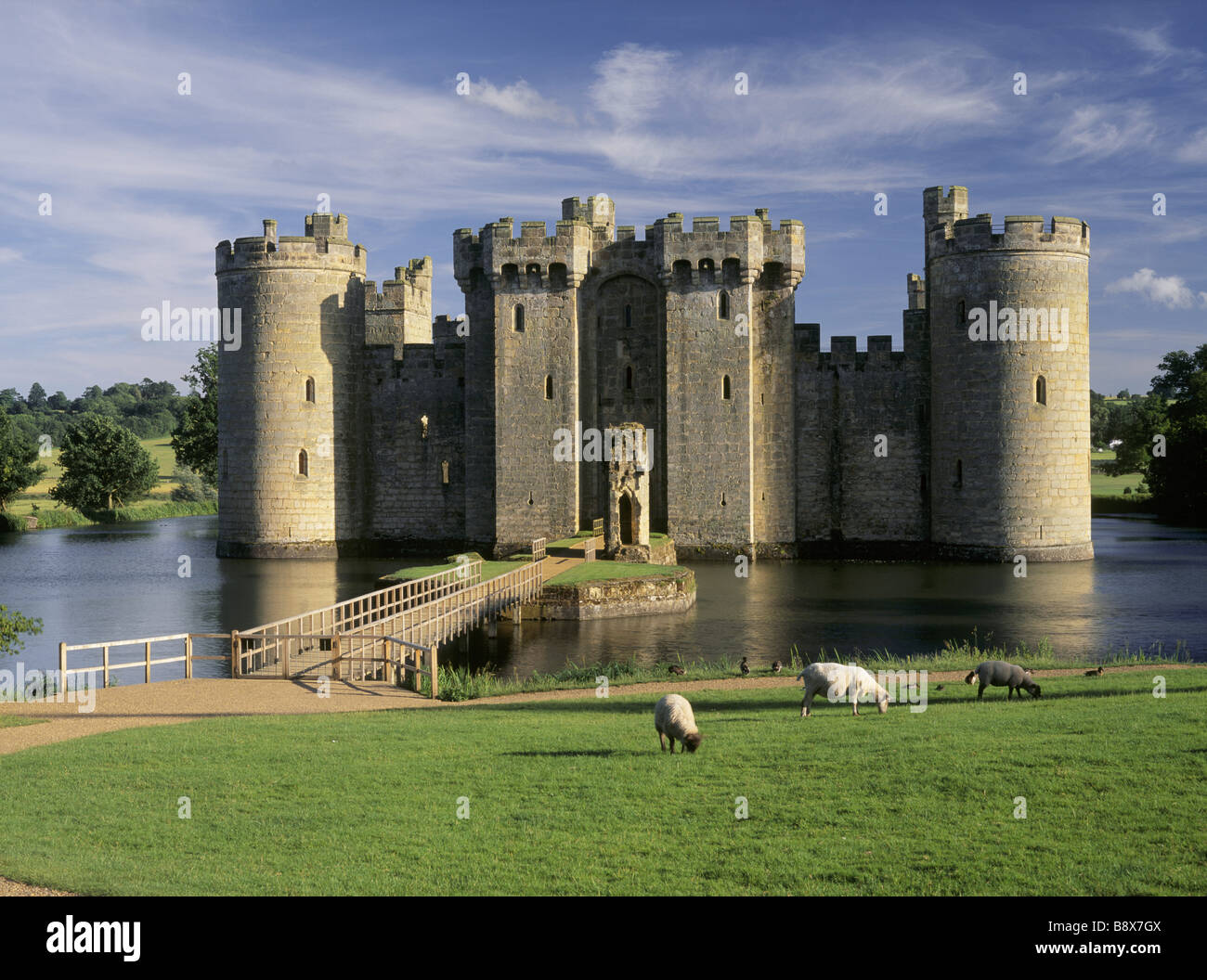 Ein Blick über die Brücke über den Burggraben Bodiam Castle einige Schafe weiden am Ufer in der Nähe von Stockfoto