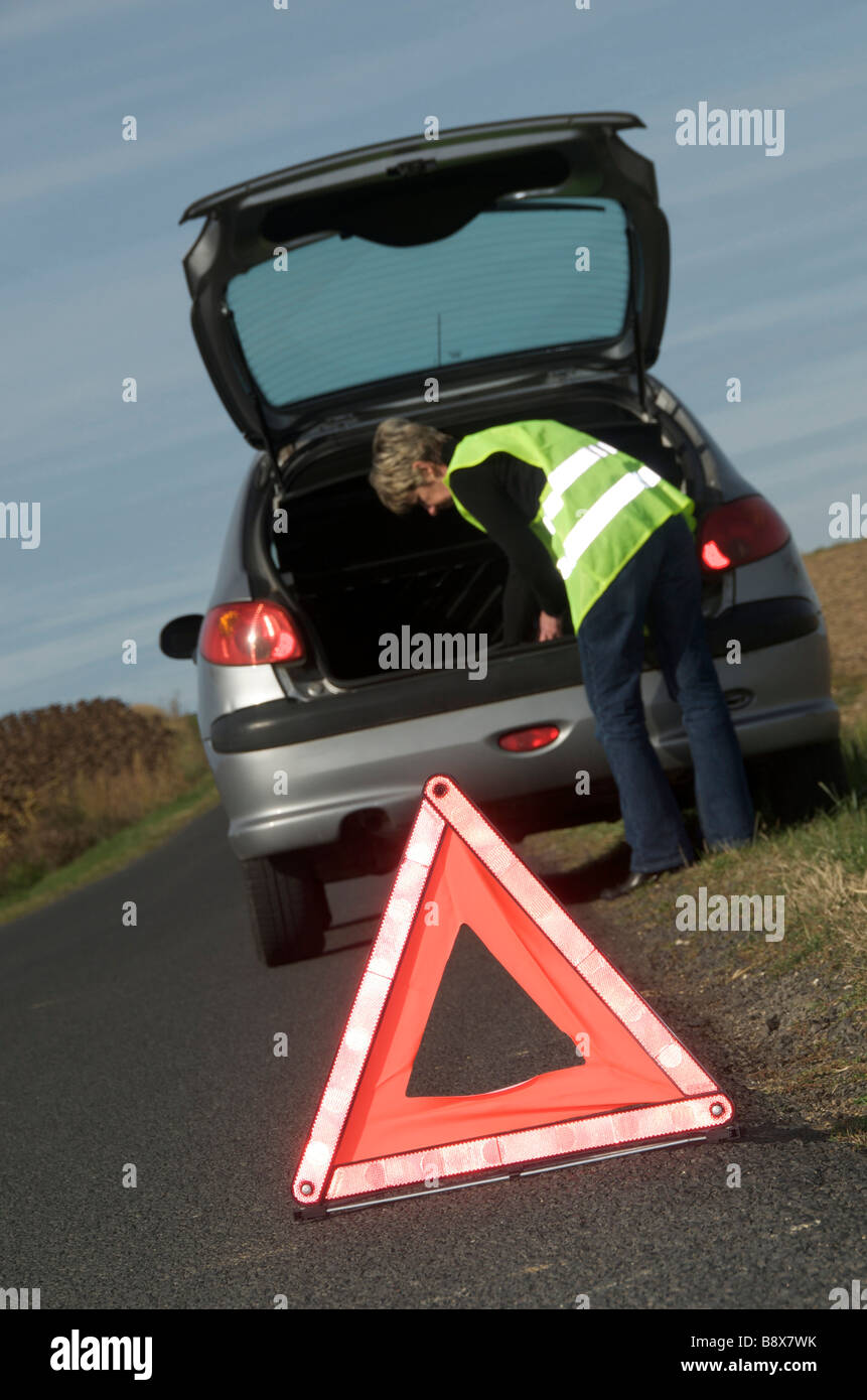 Frau mit ihr aufgeschlüsselt Auto geparkt am Straßenrand tragen gelbe hohe Sichtbarkeit / hi viz Jacke und Warndreieck Stockfoto