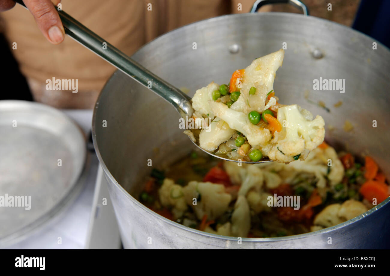 Ein Löffel Gemüsecurry rund um bedient zu werden, aus einem Topf im freien gekocht. Stockfoto