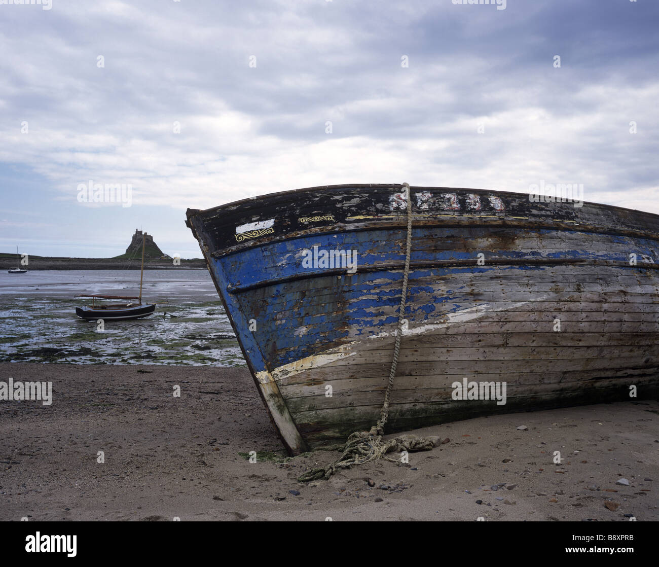 Eine Fernsicht auf Lindisfarne Burg stehen draußen in der Silhouette. Ein verfallenes Boot ruht tristement auf seiner Seite im Vordergrund. Stockfoto