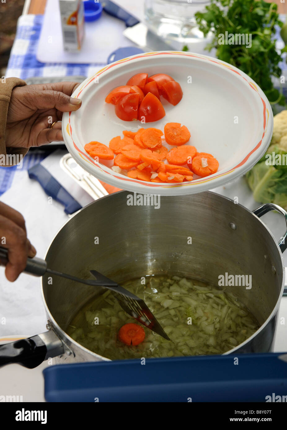 Karotten und Tomaten werden Zwiebeln in einem Topf in ein Outdoor-Gemüse-Curry hinzugefügt. Stockfoto