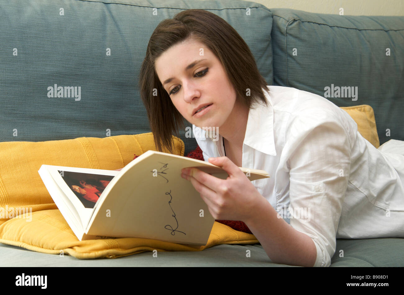 Junge Frau sucht Kunstbuch auf dem Sofa liegend / Sofa zu Hause Stockfoto