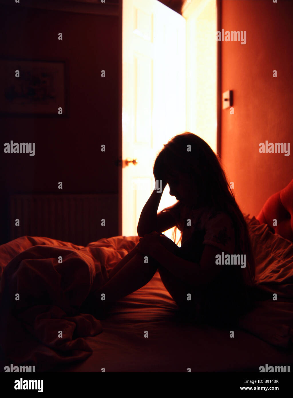 Silhouette eines jungen Mädchens in Verzweiflung in ihrem Schlafzimmer ein Licht strahlt aus außerhalb ihres Zimmers Stockfoto