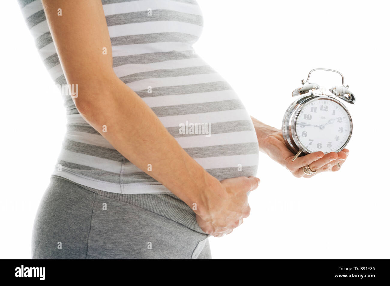 Eine schwangere Frau hält eine Uhr. Stockfoto