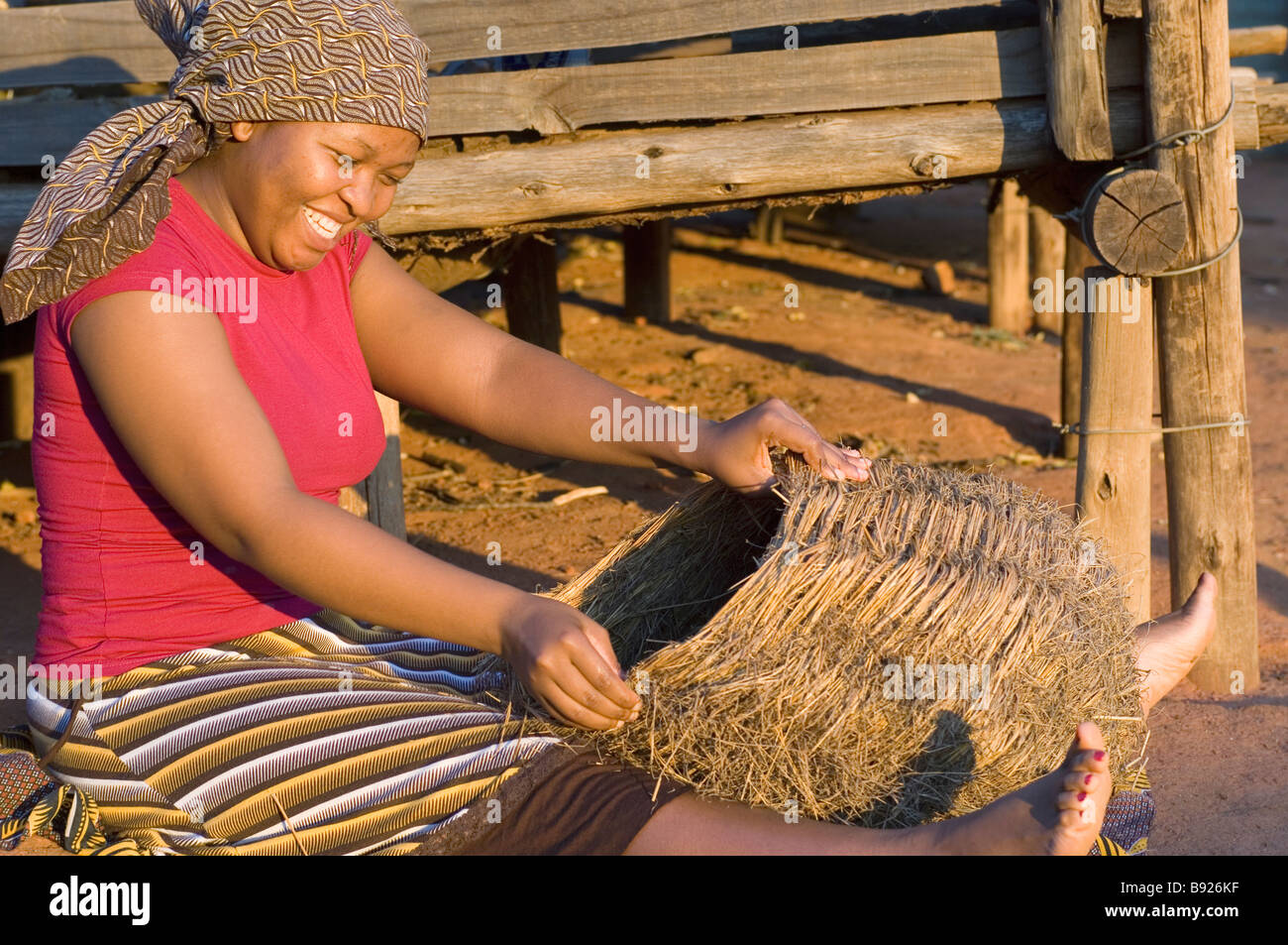 Eine lächelnde Swazi Frau arbeitet an der Herstellung eines Korbes beim Sitzen in der Sonne Swasiland Stockfoto