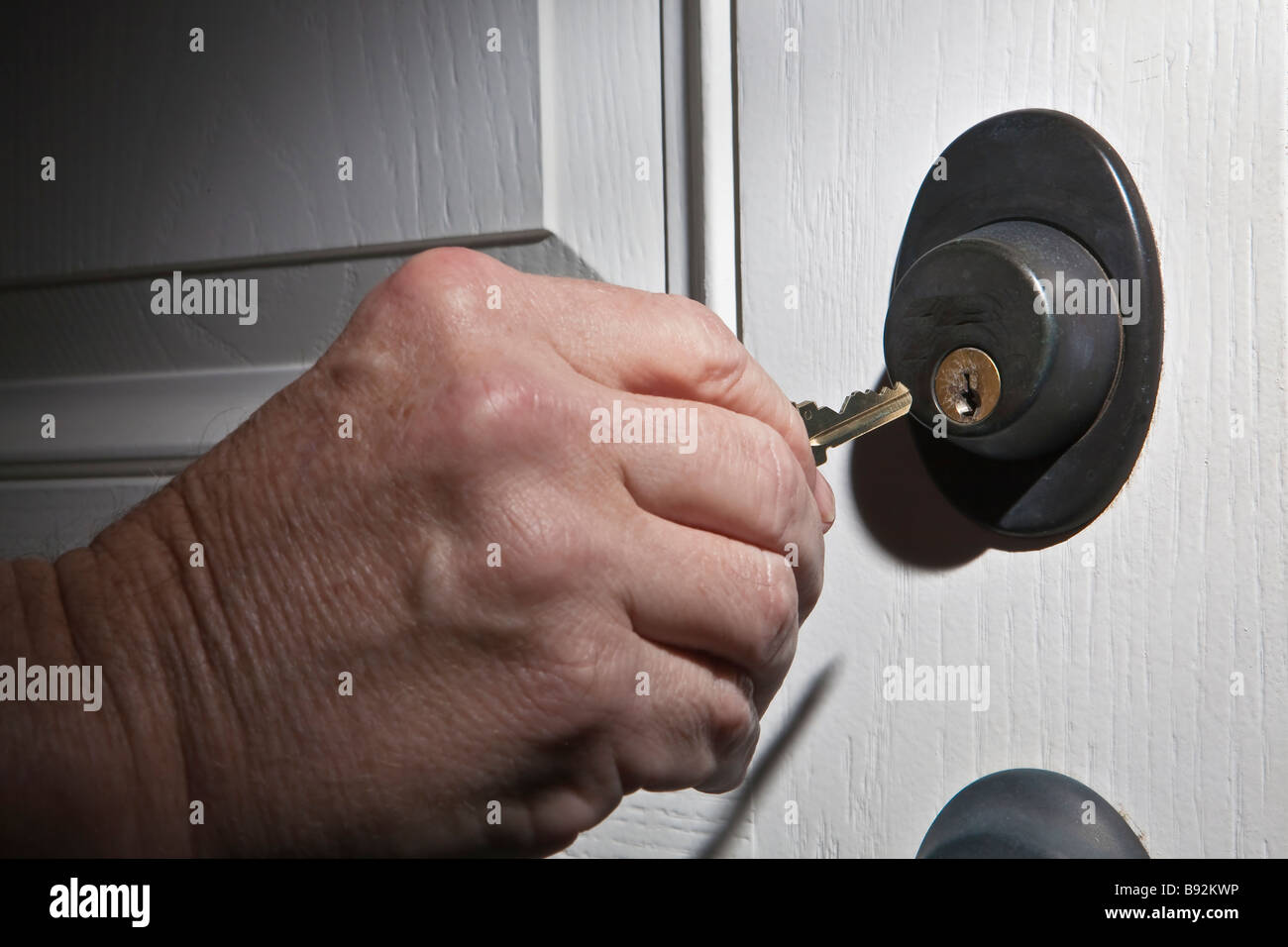 Ältere Mann s Hand unter Haus von Schlüssel oder putting Hausschlüssel in der weißen Tür sperren Stockfoto
