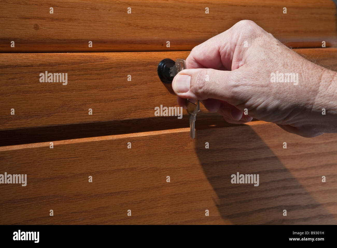 Ältere Mann s Hand drehen Schlüssel im Schloss der Schreibtisch aus Holz Stockfoto