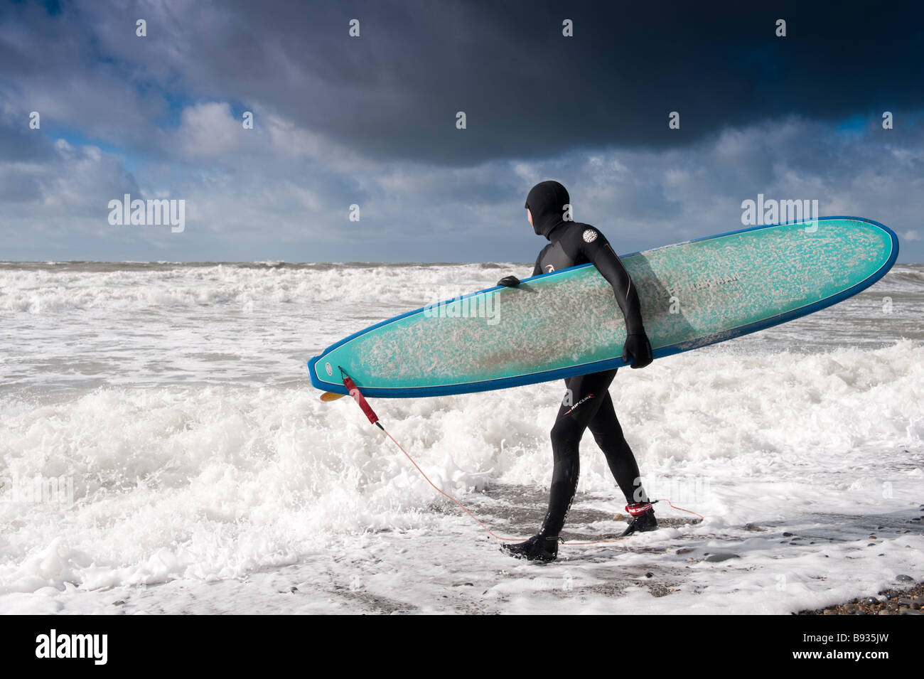 Ein Surfer Anzug nass halten Surfbrett mit Blick auf die stürmische See Aberystwyth Wales UK Stockfoto