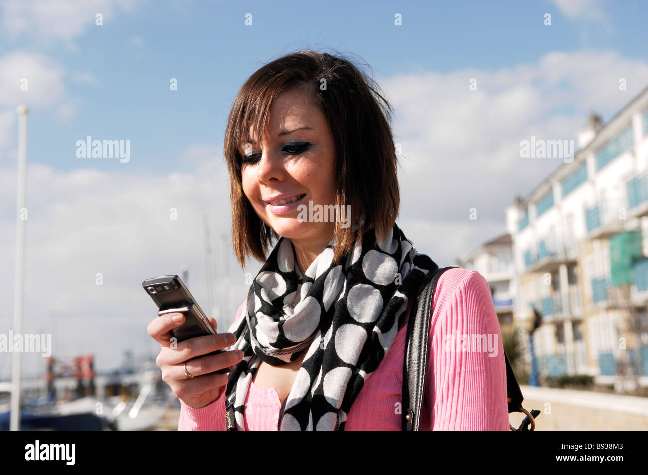 Junge Frau mit kurzen dunklen Haaren mit Handy an einem sonnigen Tag Stockfoto