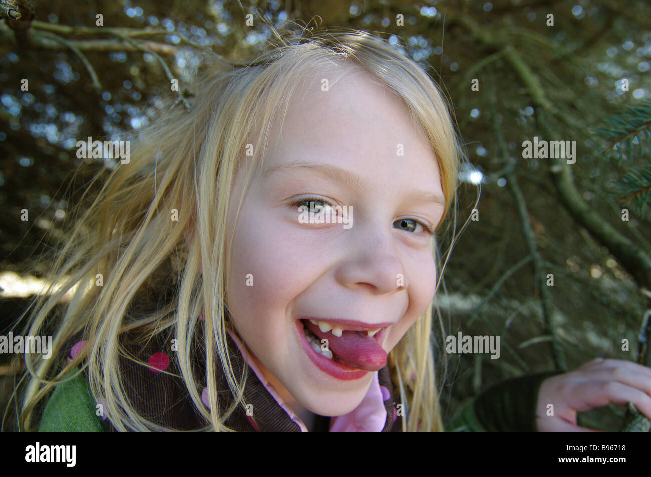 Ein lächelndes Mädchen versteckt sich in ihrem Baum Fort, ihre Zunge zwischen ihre Zähne. Stockfoto