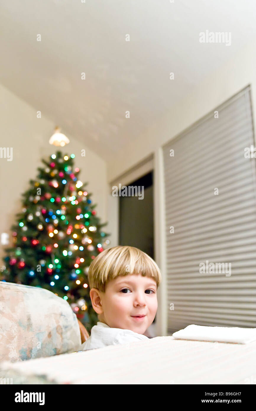 Zwei Jahre alten Jungen mit einem Weihnachtsbaum hinter ihm lächelnd Stockfoto