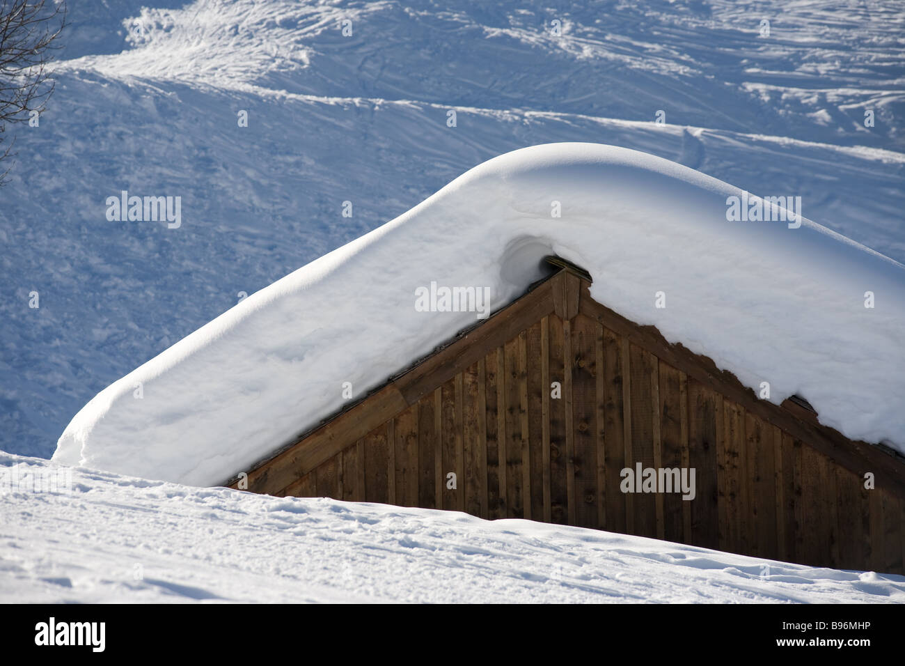 Ein dicker Mantel aus Neuschnee decken das Dach einer rustikalen hölzernen Scheune mit Skipisten in den Vordergrund und Hintergrund. Stockfoto