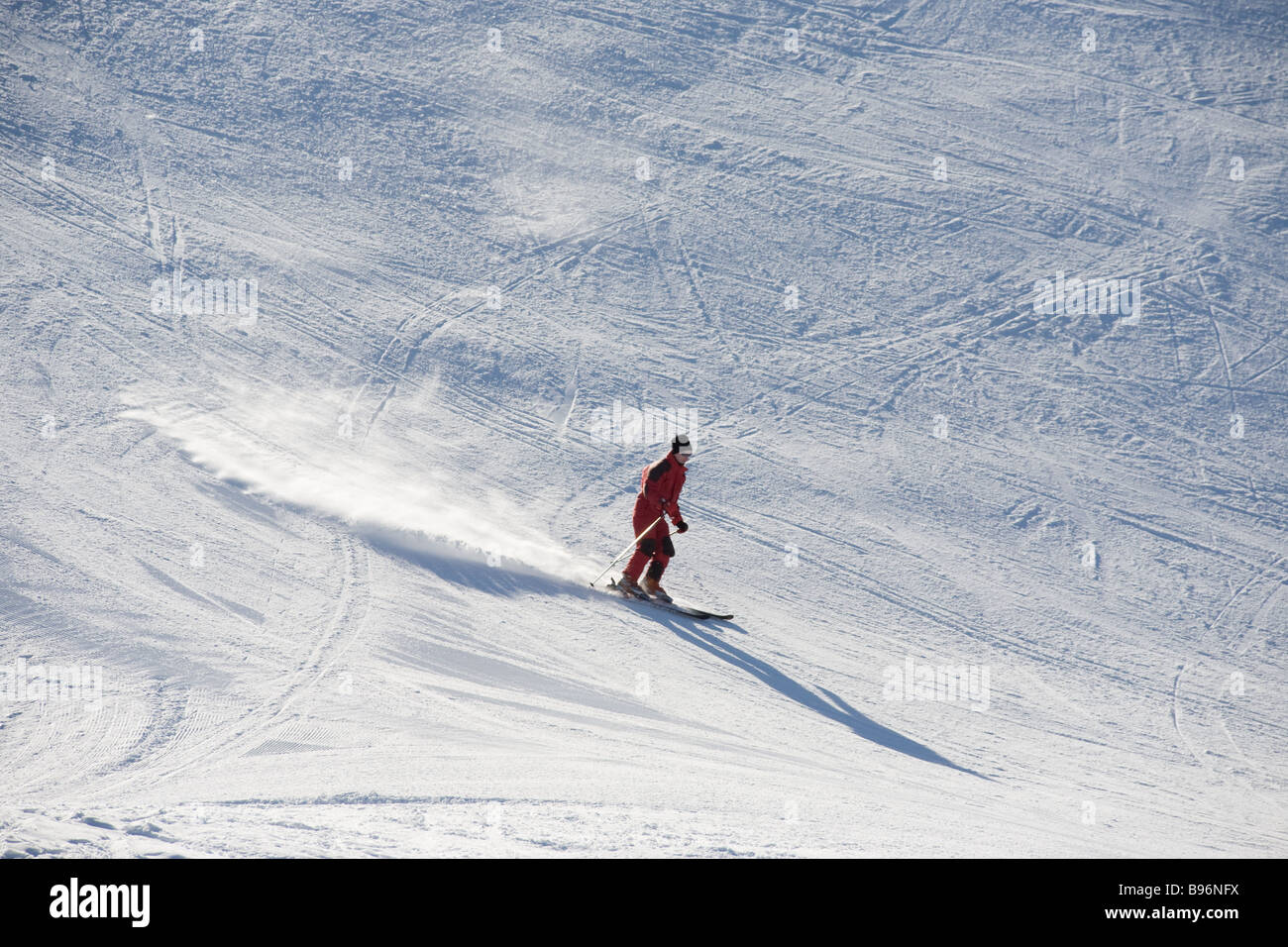 Ein einsamer Skifahrer hinunter einen Abhang in der frühen Morgensonne, die der Pulverschnee schimmert hinter ihm lange voraus Schatten Stockfoto