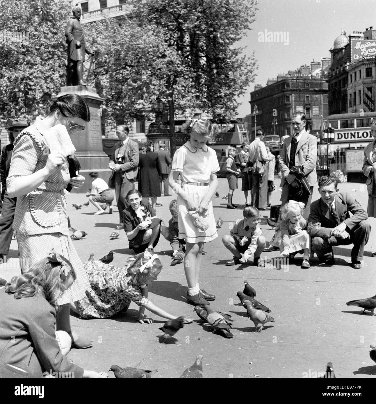 1950s, historische, sommerliche und kleine Kinder, die die Tauben auf dem Trafalgar Square, London, England füttern, beobachtet von ihren Eltern. Stockfoto