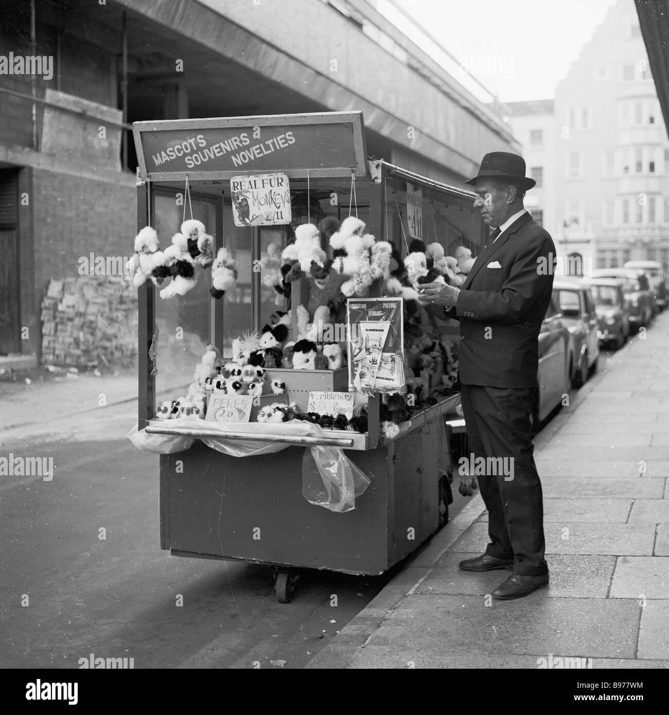 1960s, ein Straßenhändler, der an einem tragbaren Stand in einer Seitenstraße auf dem Londoner Leicester Square, England, weiches Spielzeug, Souvenirs und Neuheiten verkauft. Stockfoto