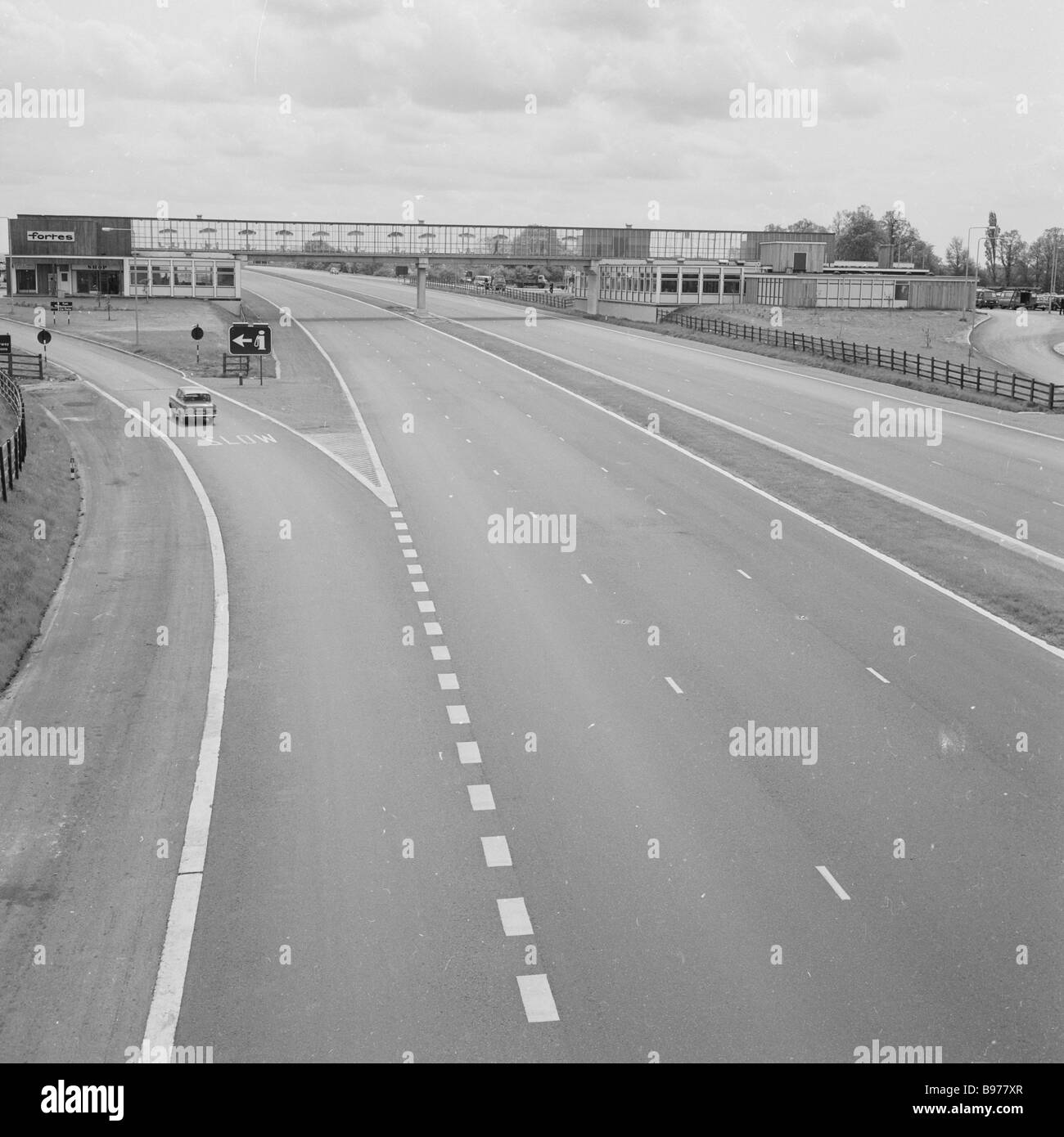 1960s, ein Auto auf einem Sliproad neben einer leeren Autobahn M1, vor einer Fortes Service Station, in Newport Pagnell, dem ersten solchen Service-Bereich in Großbritannien. Stockfoto