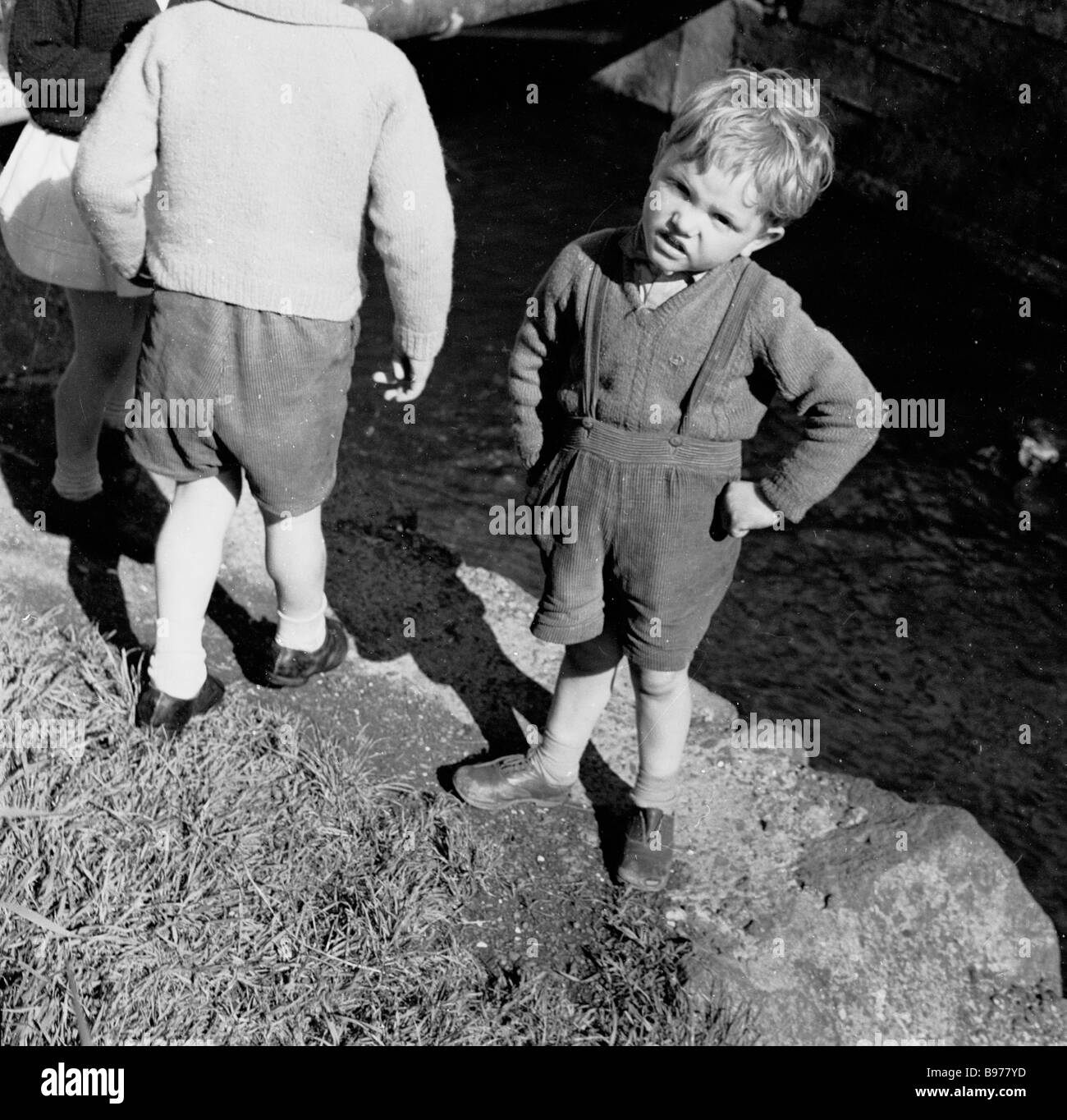 Ein kleiner irischer Junge aus den 1950er Jahren, der kurze Hosen mit Hosenträger und Händen an den Hüften trägt, besucht den Giants Causeway, Co. Antrim, Nordirland, Großbritannien. Stockfoto