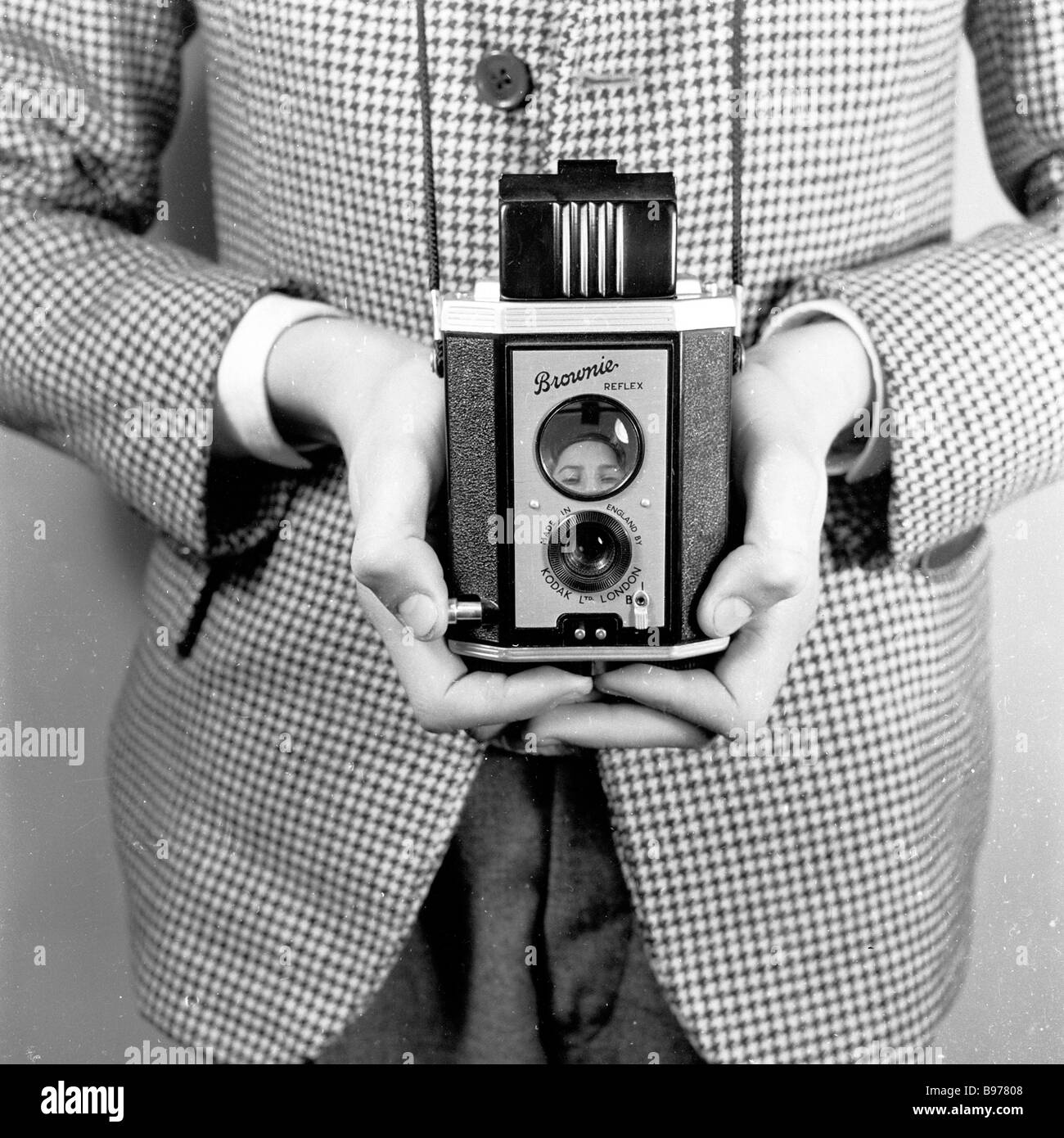 1950s, ein Junge, der demonstriert, wie man eine Kodak „Brownie“-Fotokamera mit Doppelobjektiv und Reflexionsbox hält, England, Großbritannien, mit dem Sucher oben. Stockfoto