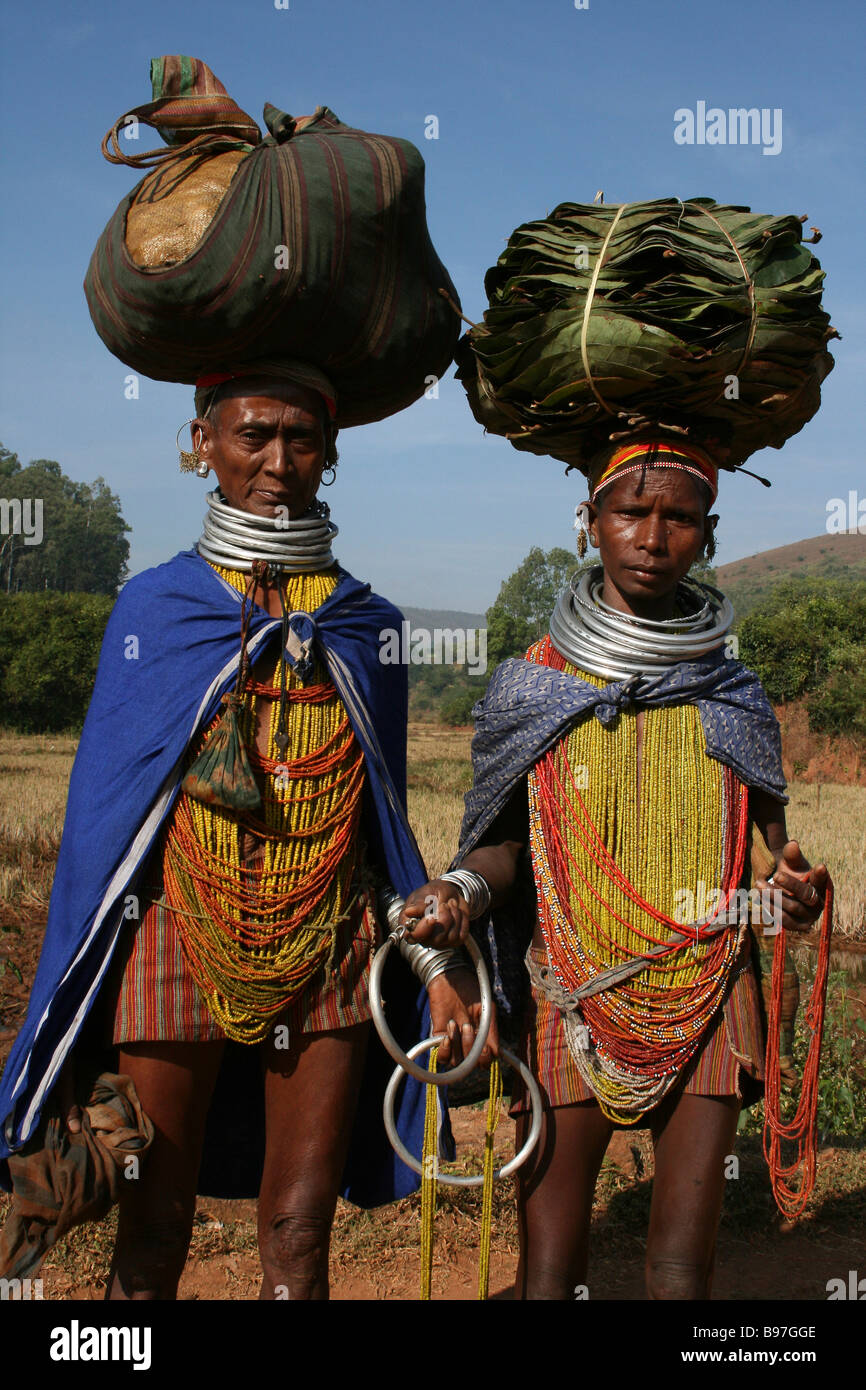 Zwei indische Bonda Stamm Frauen tragen traditionelle Perlen und Hals Ringe tragen Bündel auf dem Kopf Stockfoto