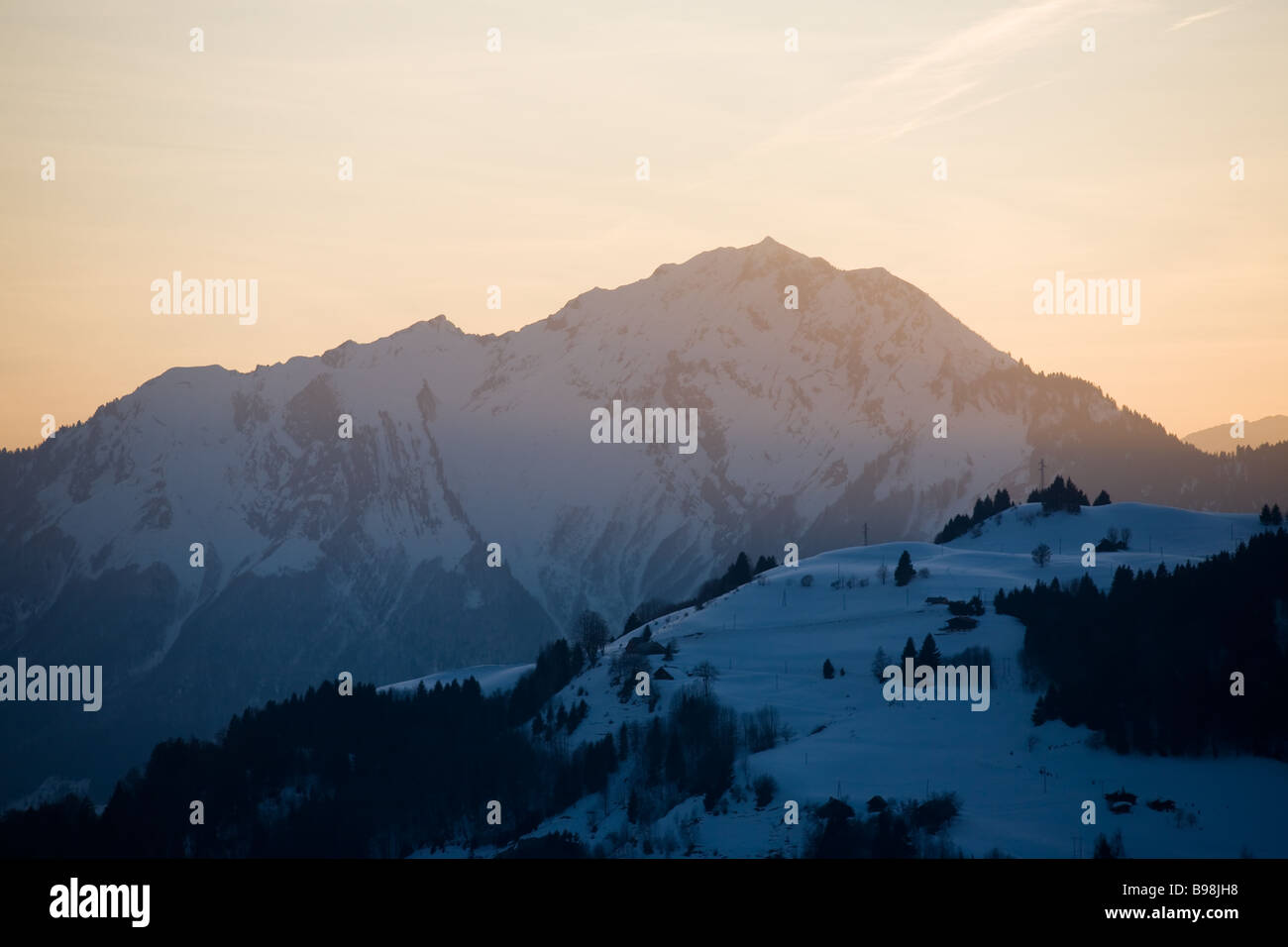 Goldener Sonnenuntergang Lichtströme über einer schneebedeckten Bergkette mit dunklen Schatten steigen aus dem Tal in den französischen Alpen Stockfoto