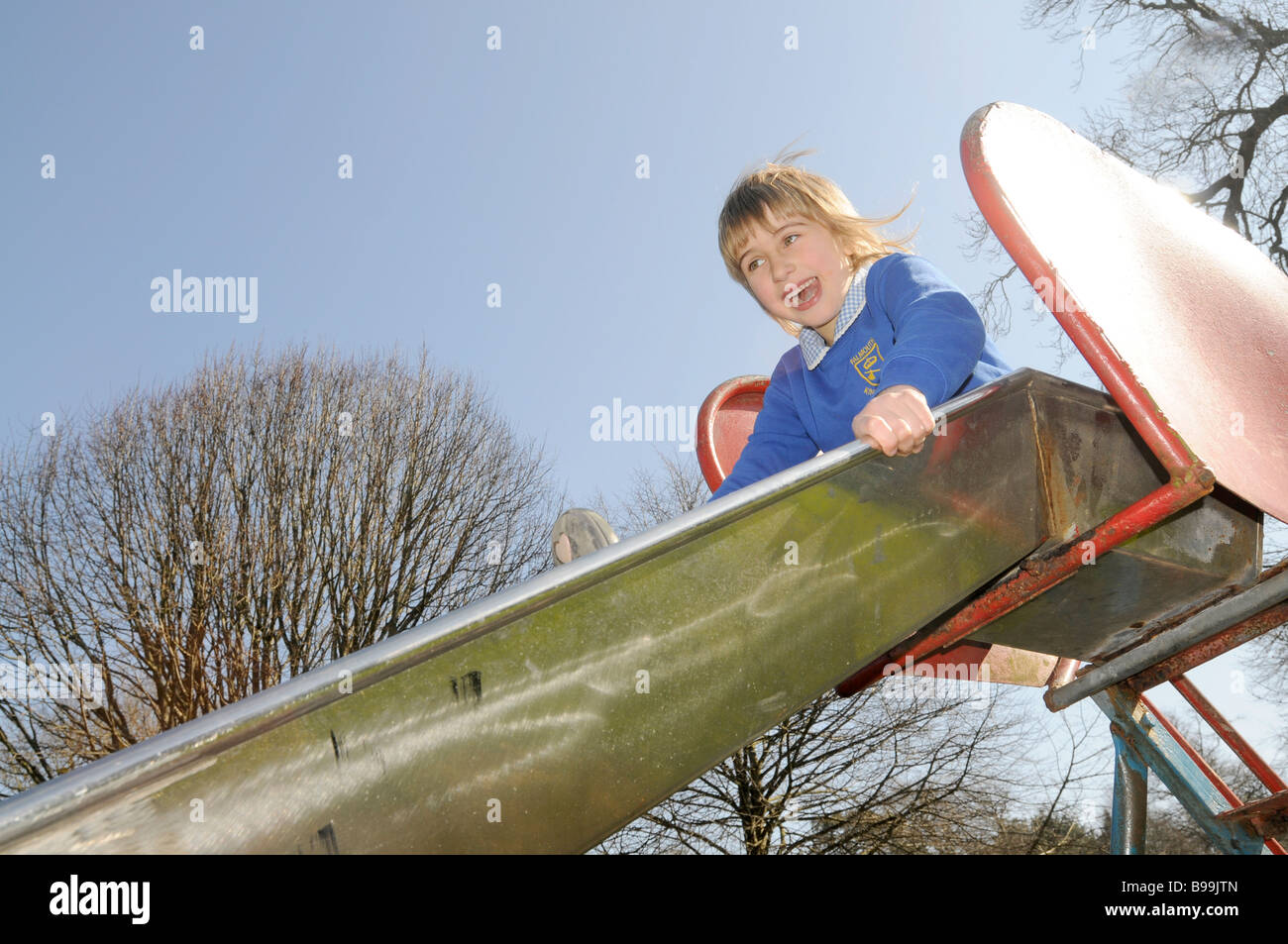 Ein sechs Jahre altes Mädchen in Schuluniform auf einer Rutschbahn Stockfoto