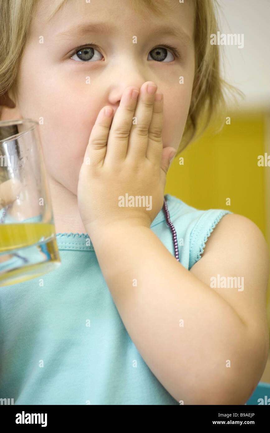 Kleines Mädchen hält Glas Saft, den Mund mit einer hand Stockfoto