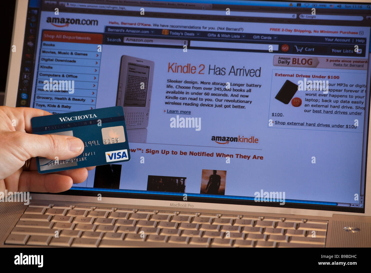 Apple Laptop-Computer-Bildschirm zeigt Internet Amazon.com Seite plus Hand mit Kreditkarte Stockfoto