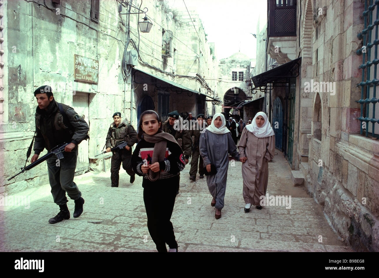 Palästinensischen Schulmädchen, gefolgt von zwei palästinensische Frauen und israelische Soldaten auf der Straße der Kette in Jerusalem, Israel. Stockfoto