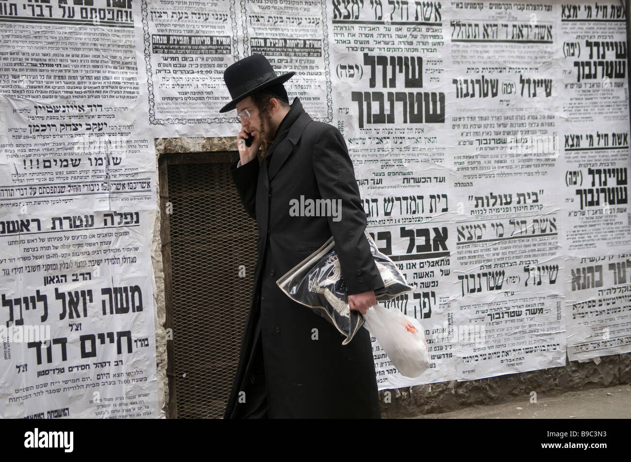 Orthodoxer Jude kommt an Paschkvilim-Broadside-Plakaten vorbei, die als Gemeinschaftsankündigungen im Viertel Mea Shearim Haredi in Jerusalem Israel dienen Stockfoto
