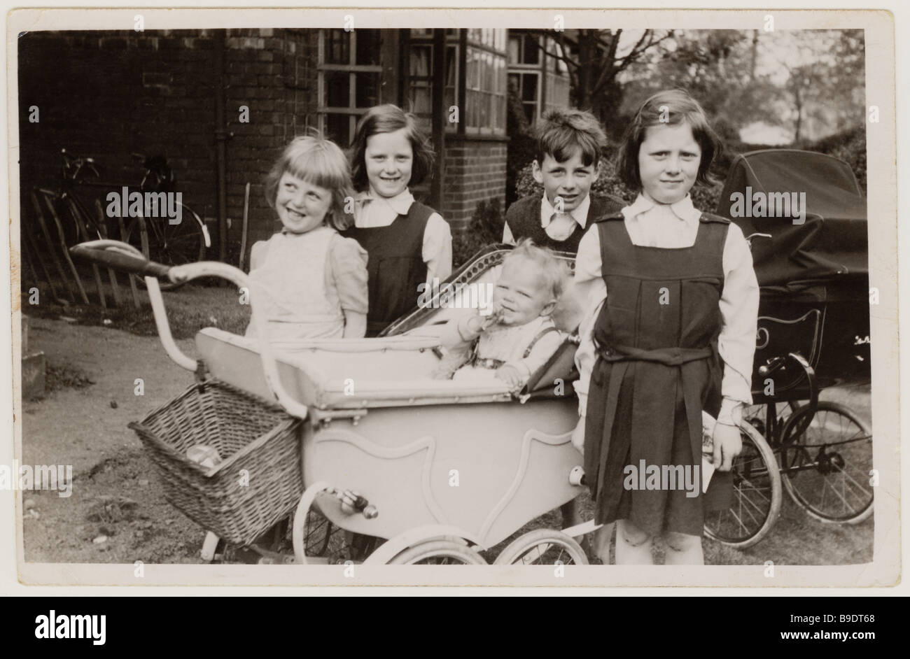 Freche junge Schulkinder mit Kinderwagen, die sich außerhalb ihres Hauses um ein Baby in den 1950er Jahren, Großbritannien, kümmern Stockfoto