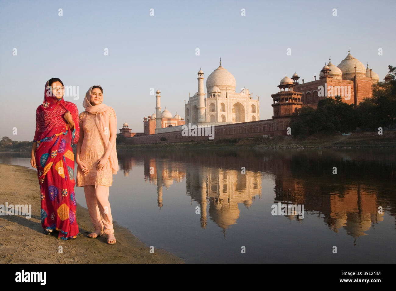 Zwei Frauen stehen am Ufer des Flusses mit einem Mausoleum in den Hintergrund, Taj Mahal, Agra, Uttar Pradesh, Indien Stockfoto