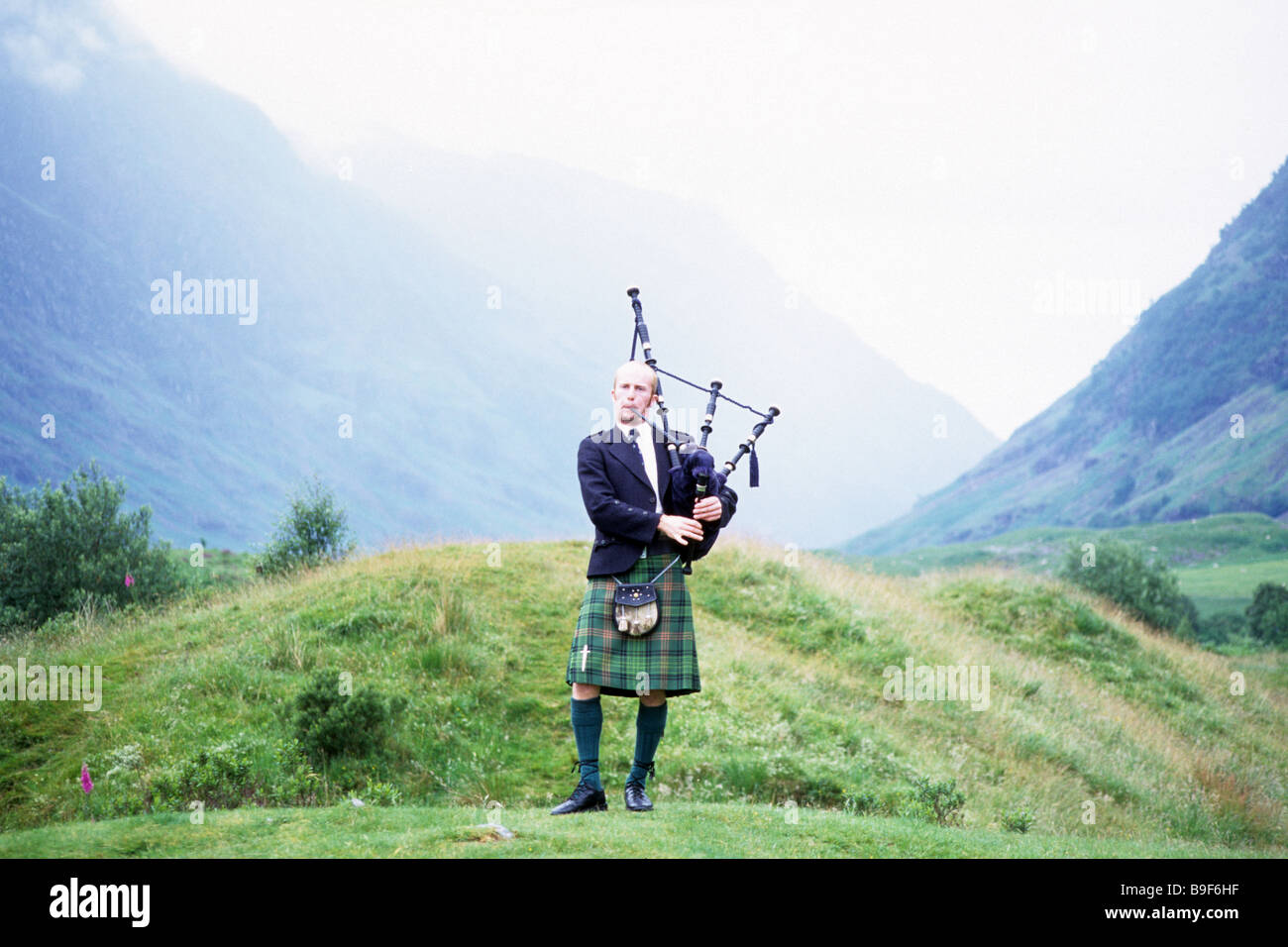Scottish Piper in einem nebligen Glen, Scotland, UK Stockfoto
