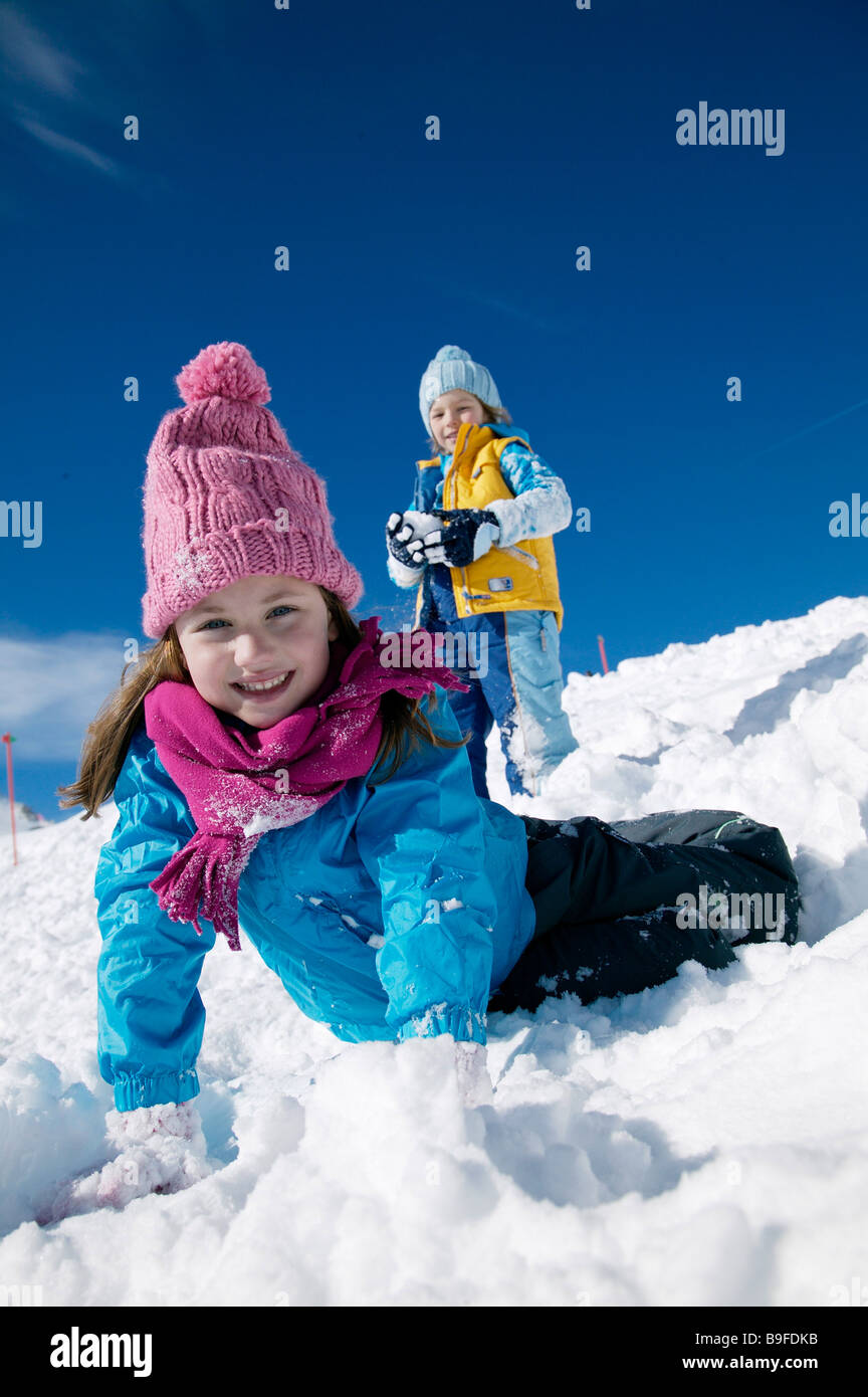 Porträt von Mädchen am Schnee liegen und lächelnd mit Junge stand im Hintergrund Stockfoto