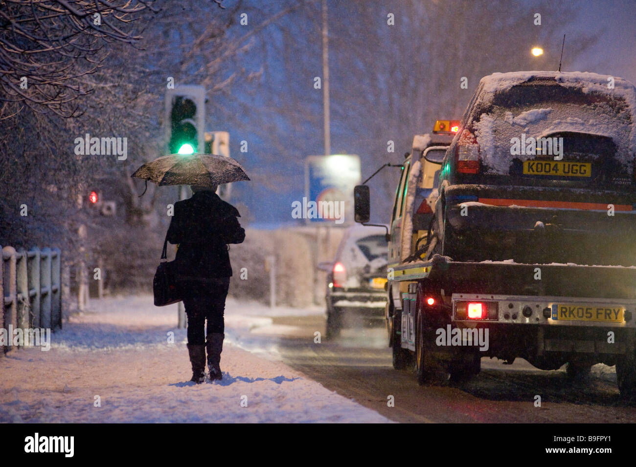 Lady Heimweg von der Arbeit entlang einer schneebedeckten Fahrbahn an einem Wintertag in england Stockfoto