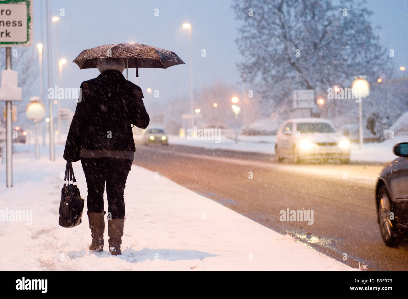 Lady Heimweg von der Arbeit entlang einer schneebedeckten Fahrbahn an einem Winter-Abend in england Stockfoto