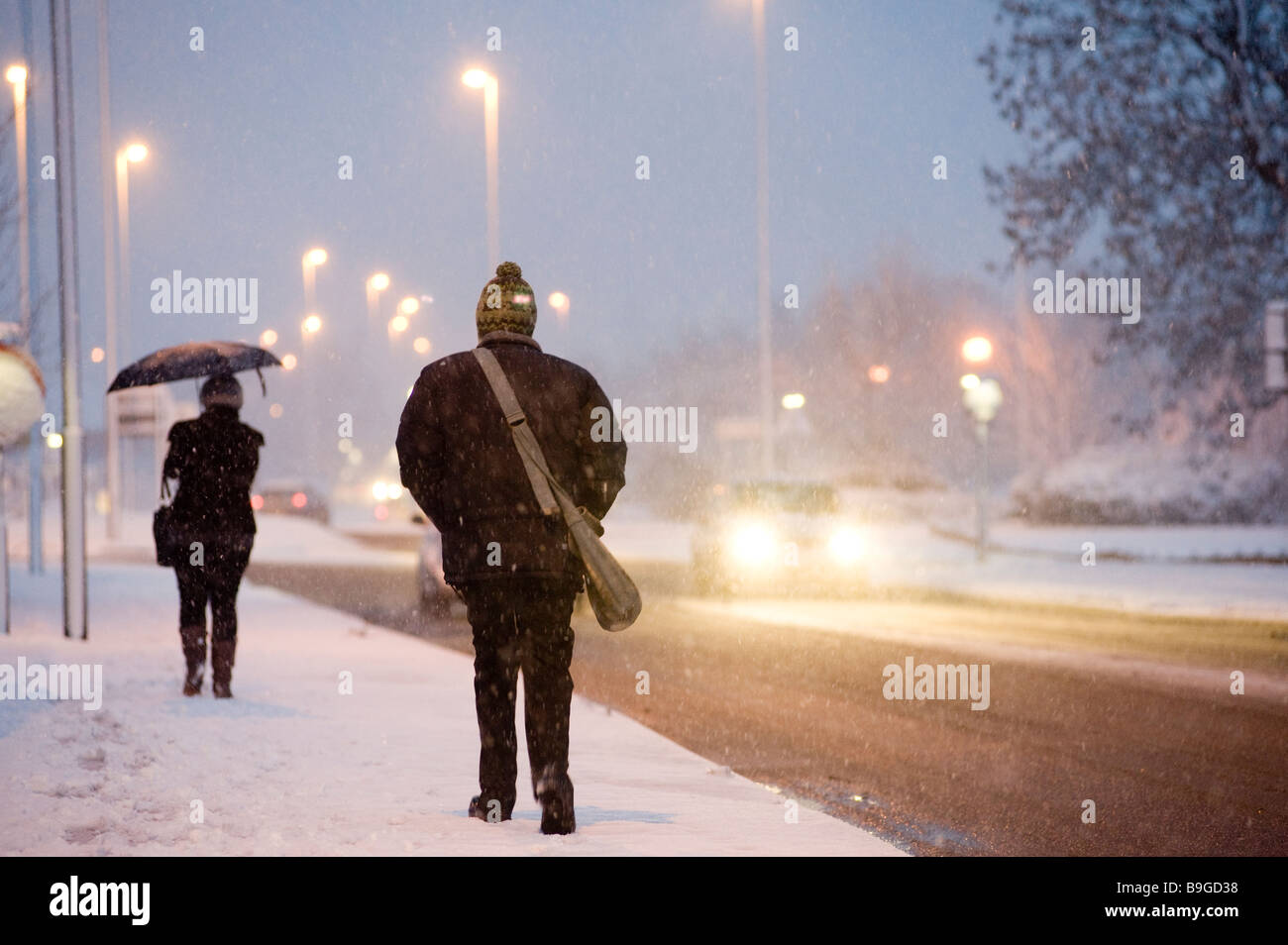 Menschen, die zu Fuß zur Arbeit entlang einer schneebedeckten Fahrbahn an einem Winter-Abend in england Stockfoto