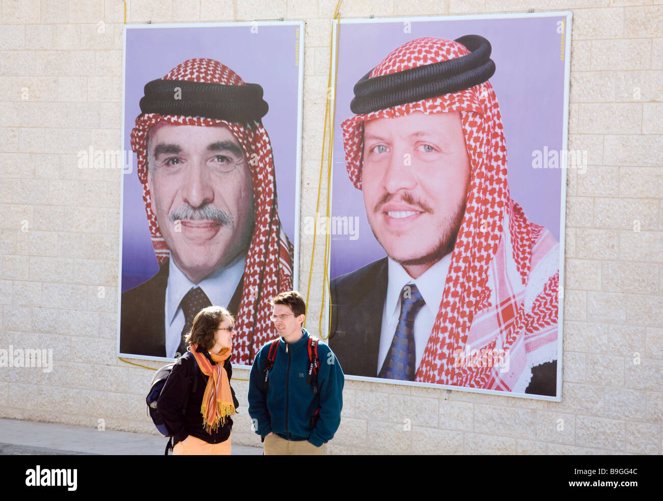 Ein paar Touristen sprechen vor Poster von König Hussein und sein Sohn, König Abdullah von Jordanien; Jordan, Middle East Asia Stockfoto