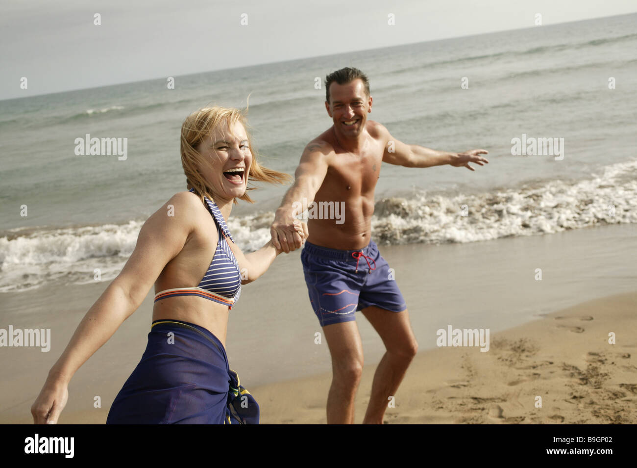 Paaren läuft angebrochenen See fröhlich miteinander einher Strand 41 Jahre 44 Jahre thematisiert außerhalb äußere Stämme Bad-Kleidung Stockfoto