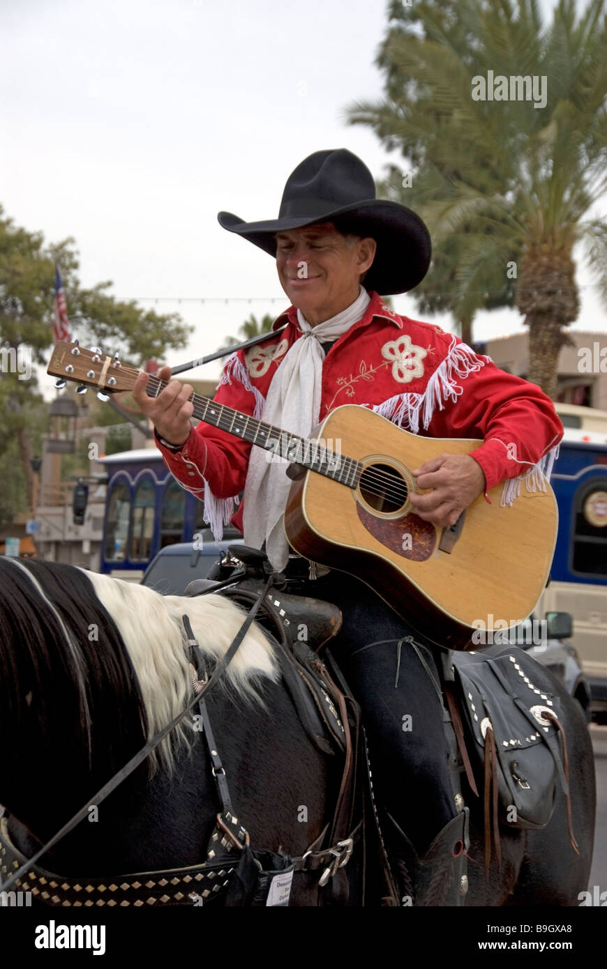 Cowboy in die Altstadt von Scottsdale Arizona und spielt seine Gitarre beim Reiten ein Pferd-Shops sind hinter ihm. Stockfoto