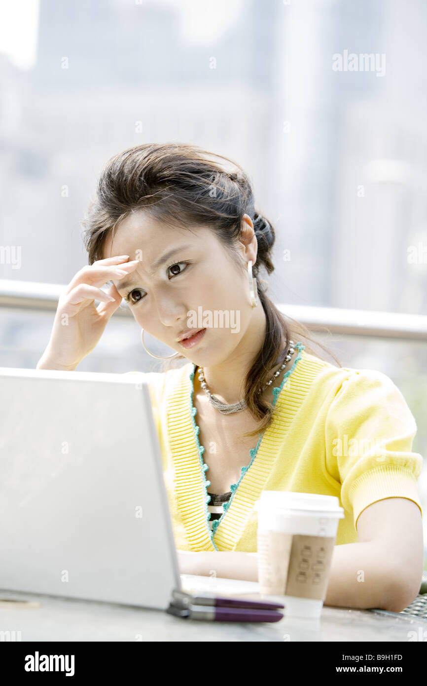 Eine junge Frau mit Kopf in der hand mit Blick auf Laptop im Café Porträt Stockfoto