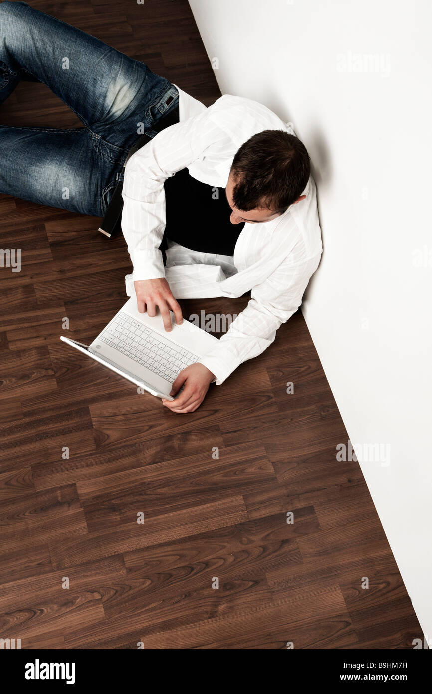 Junger Mann auf dem Boden sitzend auf seinem Laptop, Luftperspektive Stockfoto
