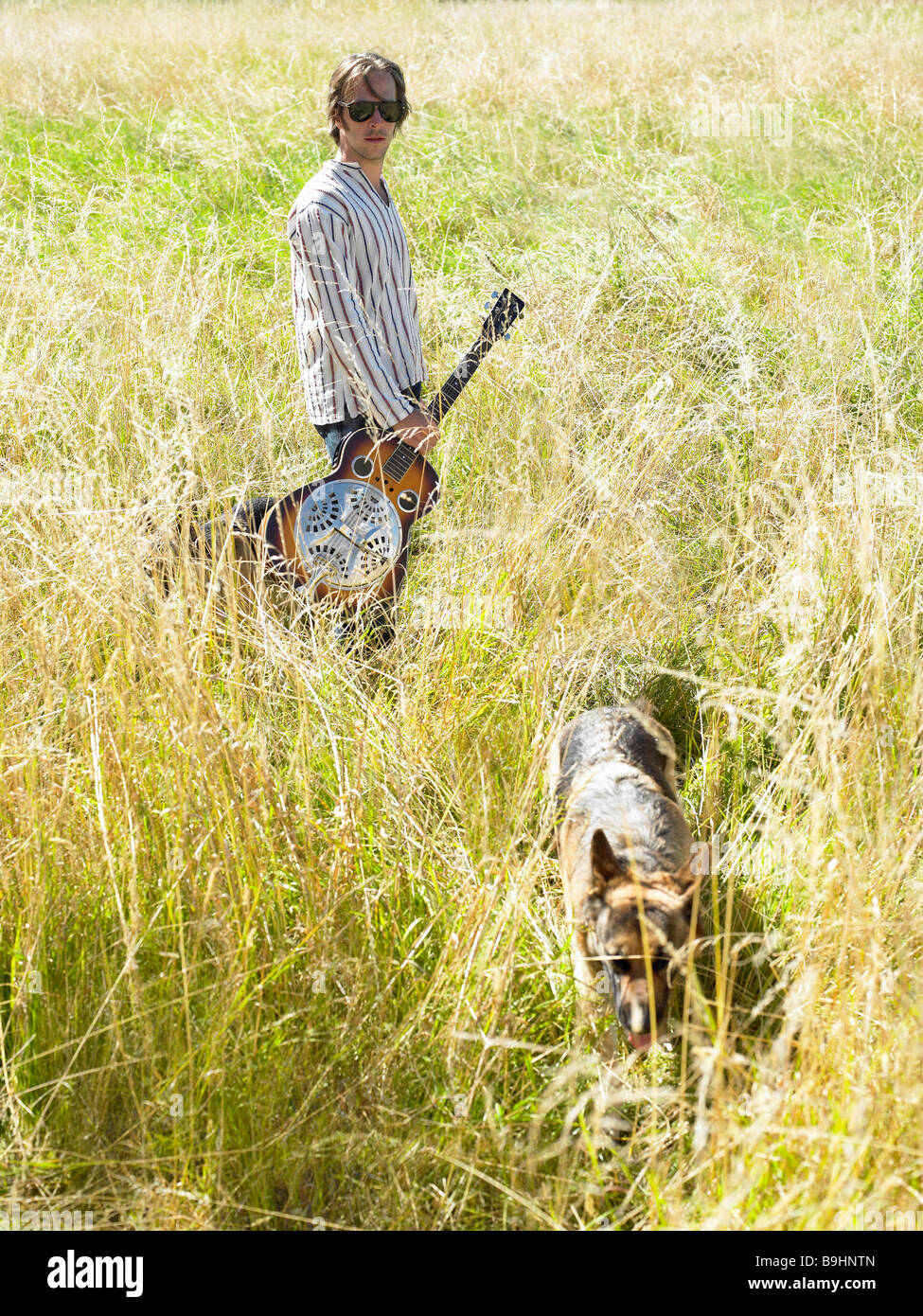 Mann mit seiner Gitarre und seinem Hund in einem Feld Stockfoto