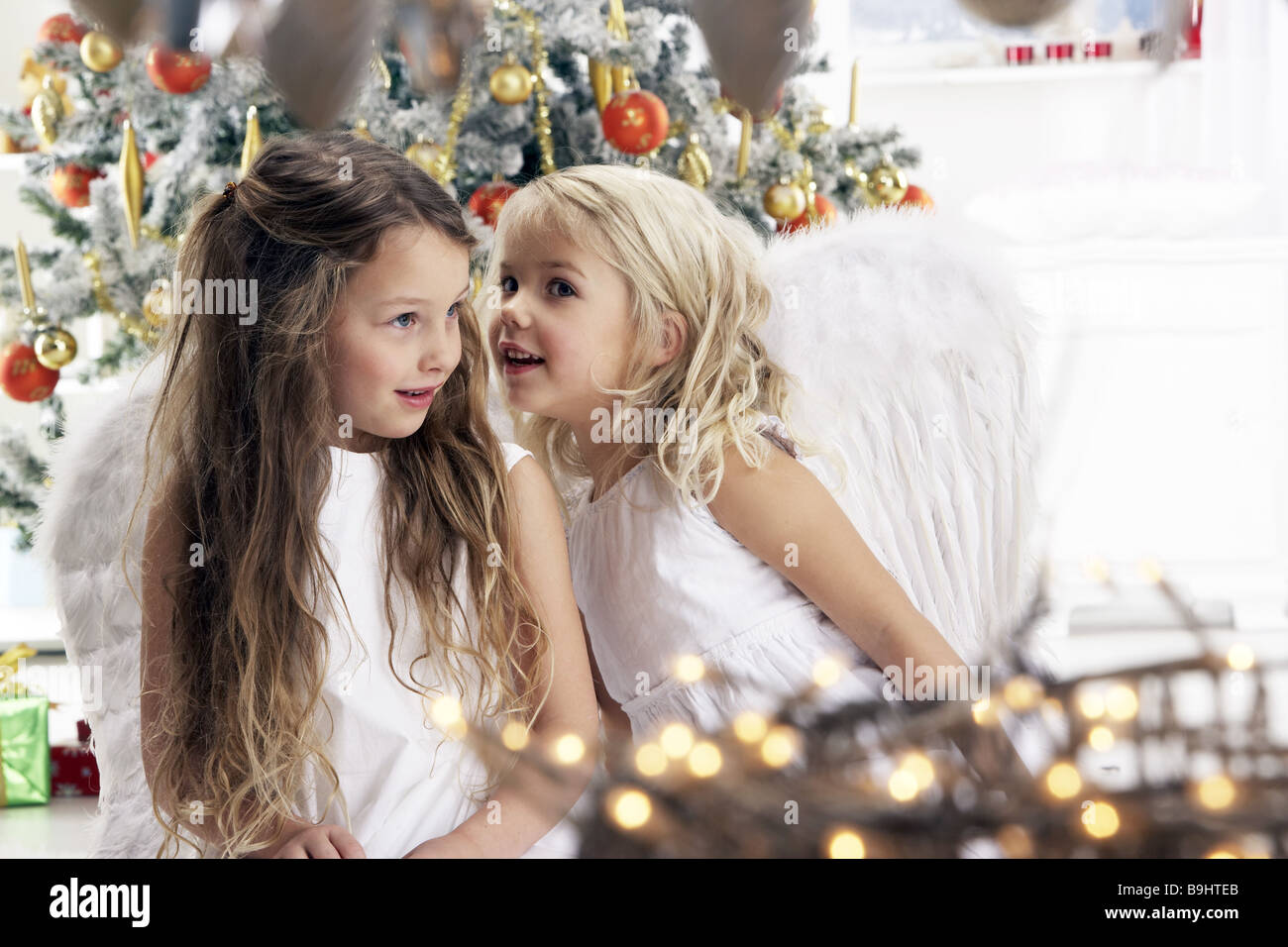 Weihnachten Living Zimmer Kinder Mädchen Engelsflügel outfit Weihnachtsengel flüstert semi-Porträt Menschen Schwestern Geschwister Freunde Stockfoto