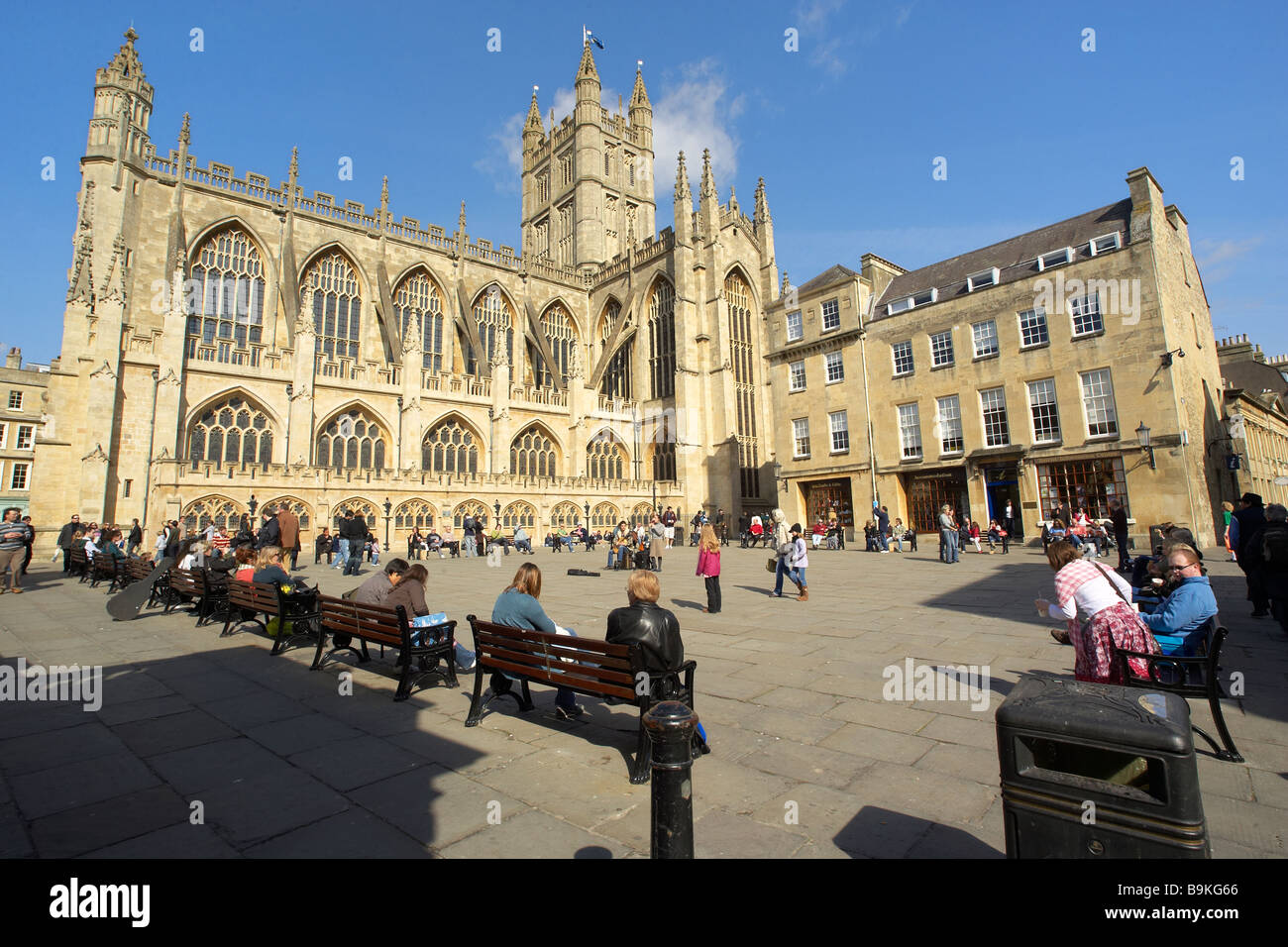 Leute sitzen in der Sonne beobachten ein Straßenmusikant außerhalb Bath Abbey in Bath durchführen somerset uk. Stockfoto