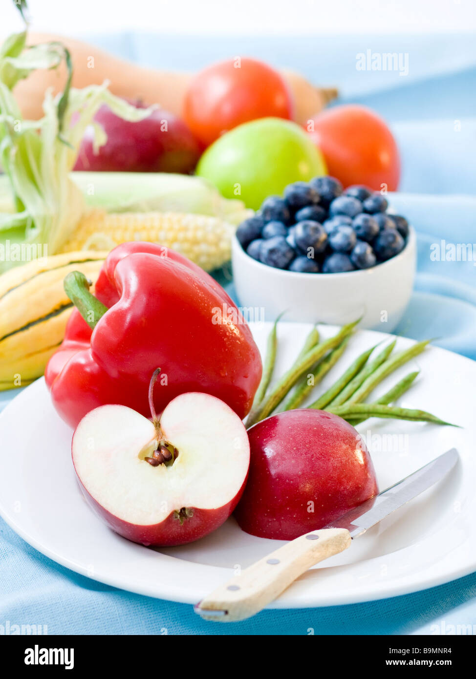 Nahaufnahme von geschnittenen Äpfeln und Paprika in Plage mit frischem Obst und Gemüse im Hintergrund Stockfoto