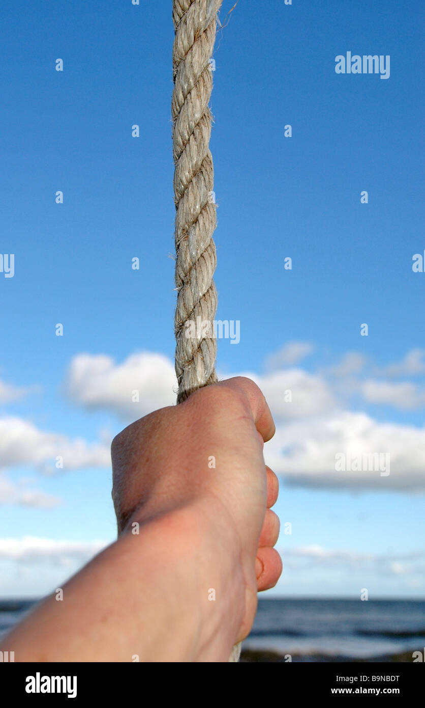 Eine Hand greifen einen abgesenkten Seil mit dem Meer im Hintergrund. Stockfoto