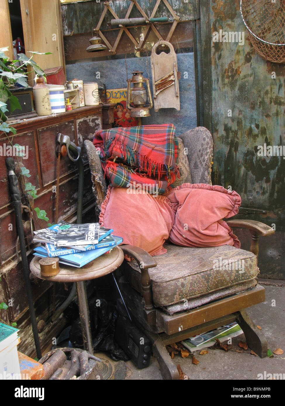 Schaukelstuhl mit Kissen und Lesetisch im mit Schrott gefüllten Gartenschuppen - eine echte Menschenhöhle Stockfoto