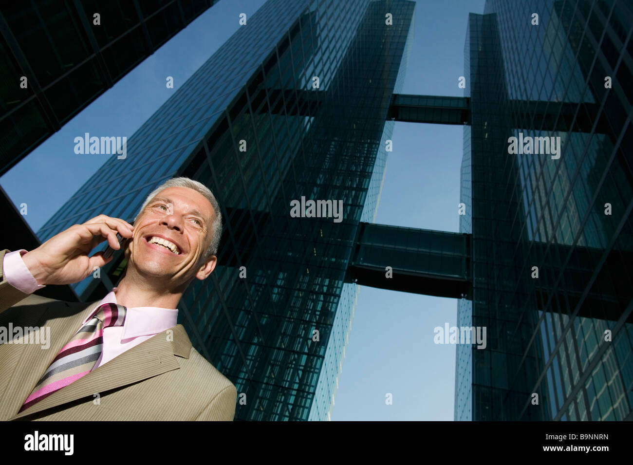 niedrigen Winkel Porträt von reifer Geschäftsmann telefonieren mit Handy vor Bürogebäude Stockfoto